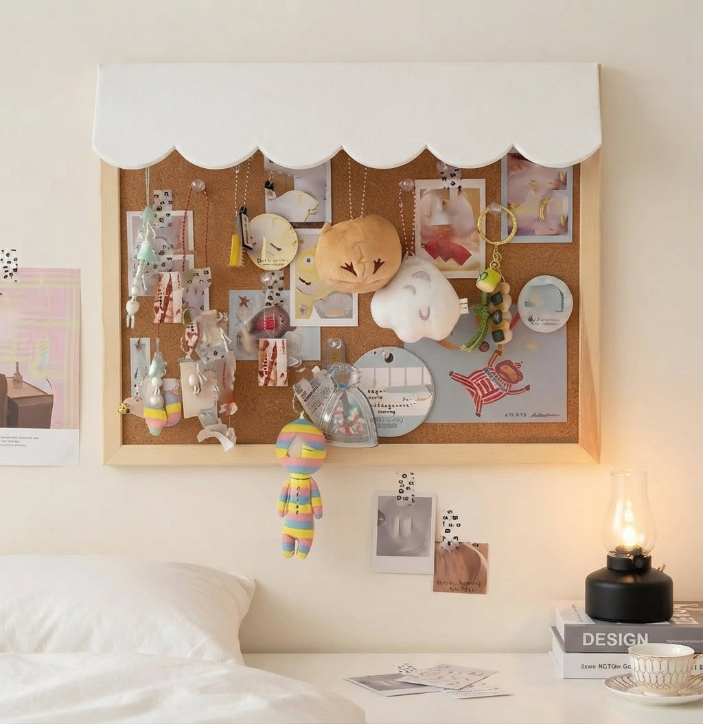 A cloud-shaped cork bulletin board with a white fabric top, mounted on a bedroom wall above a bed. The board is decorated with photos, sticky notes, a small plush toy, and hanging accessories.