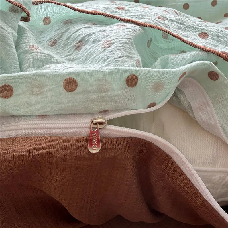 A close-up of a crinkled muslin fabric bedding set in soft mint green and dusty rose, featuring a polka dot pattern, a white zipper, and a visible 'ESPRIT' brand pull tab.